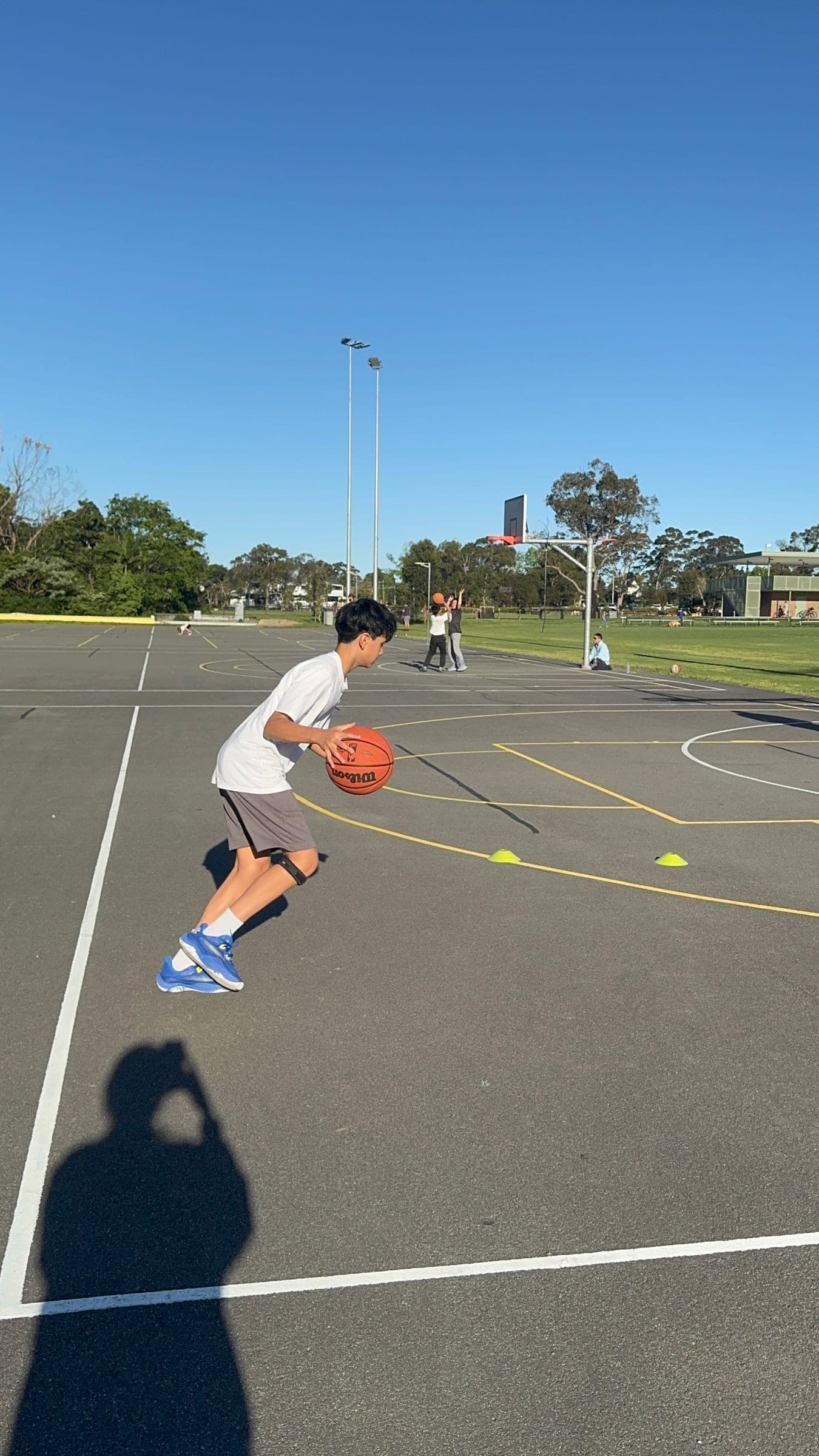 Ethan dribbling a basketball on an outdoor court, wearing a knee strap